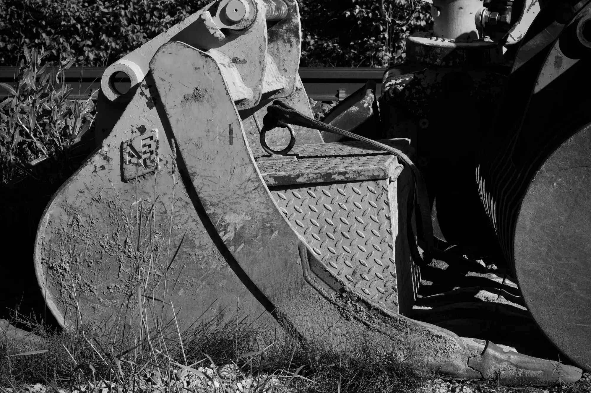 Black-and-white close-up of an excavator bucket resting in long grass